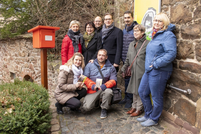 von links, hintere Reihe: Stempelpatin Petra Krapp, Schriftstellerin Kathrin R. Hotowetz, Verleger Axel Steinbach, Tobias Kascha, Andreas Meling (Leiter Stadtbetriebsamt Wernigerode), Sabine Krüger (Leiterin Tourist-Information Wernigerode) und Nicole Becker freuen sich gemeinsam mit Jacqueline Wiedener (untere Reihe links, Leiterin Souvenir- und Publikationsverkauf, Schloss Wernigerode) und Fotograf Stefan Herfurth über den neuen Stempelkasten
© Winnie Zagrodnik